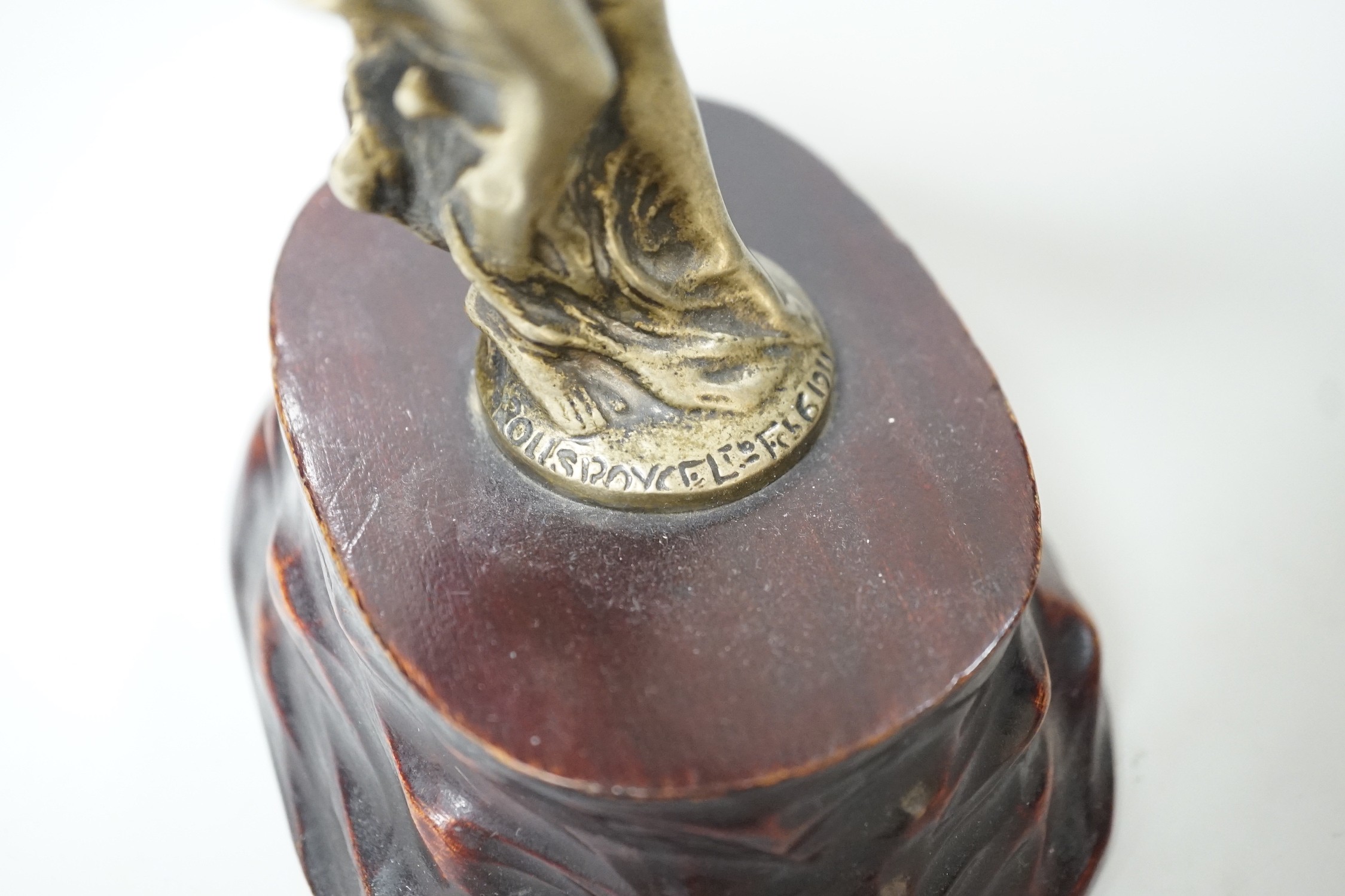 After Charles Sykes, a gilt metal Rolls Royce car mascot - ‘’Spirit of Ecstasy’’, inscribed and bearing date 1911, on a carved wooden plinth. 17.5cm tall